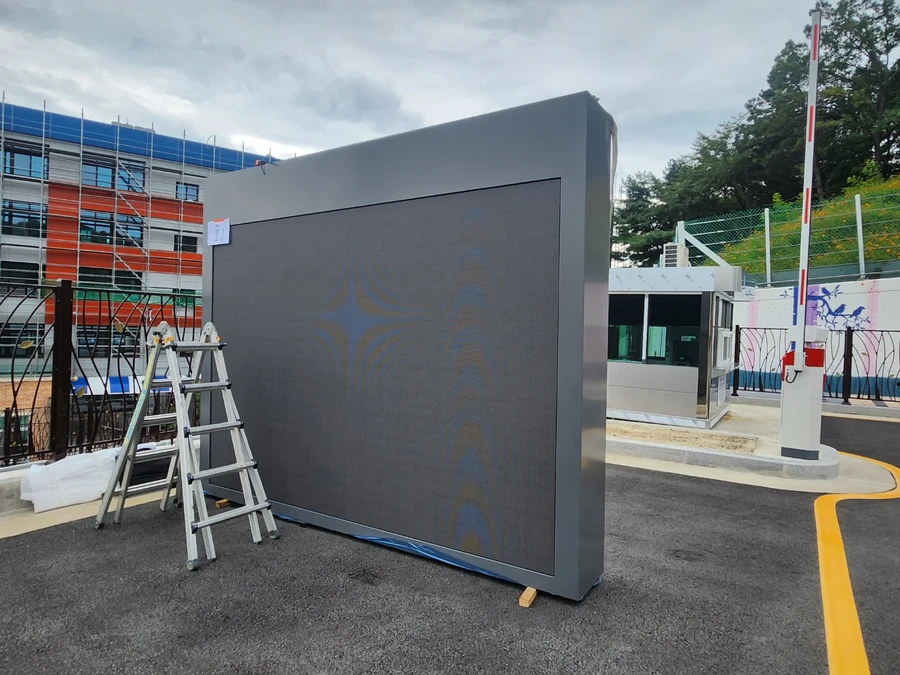 이동식 LED 전광판 참고 - 지면에 세워 둔 회색 대형 LED 전광판 캐비닛과 접이식 사다리
