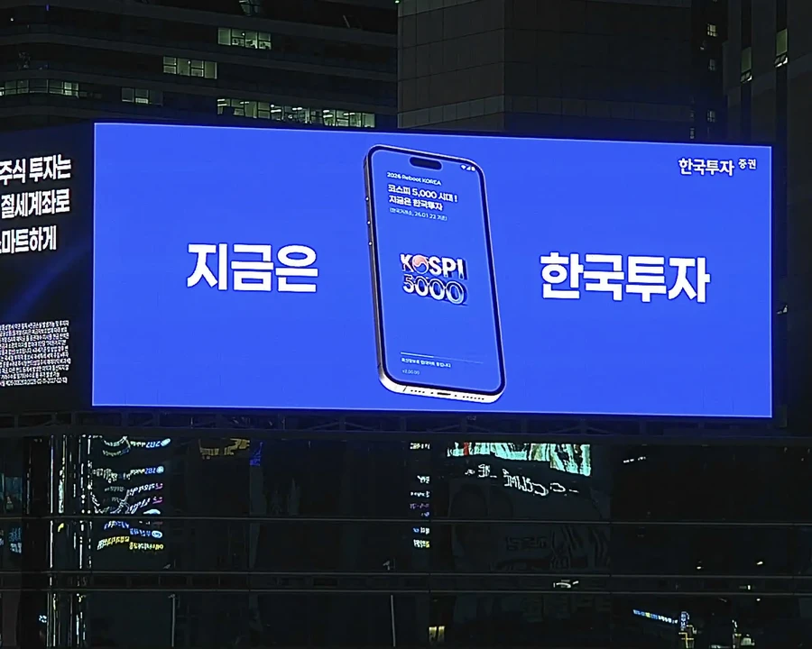서울 도심 어두운 건물 외벽에 큰 파란 화면으로 광고 문구가 표시된 LED 전광판